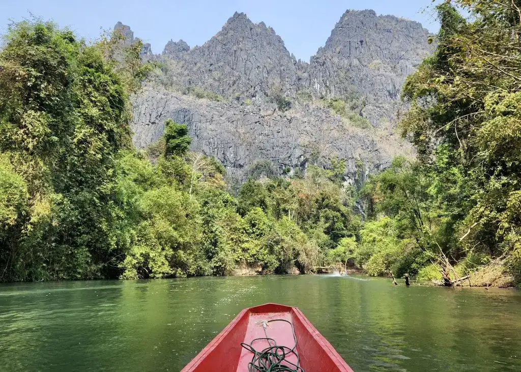 Laos or Vietnam: How to Choose the Best Country for Your Trip 20 A red boat emerging from Kong Lor Cave along a river surrounded by trees and a mountain