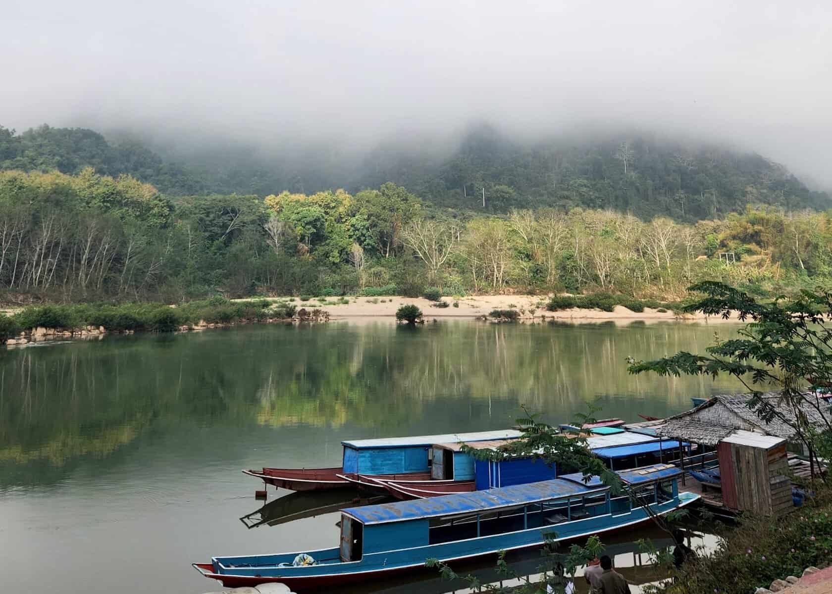 Laos 9 A longboat on a river in the morning waiting for the public boat from Muang Ngoi. There is fog covering the mountains