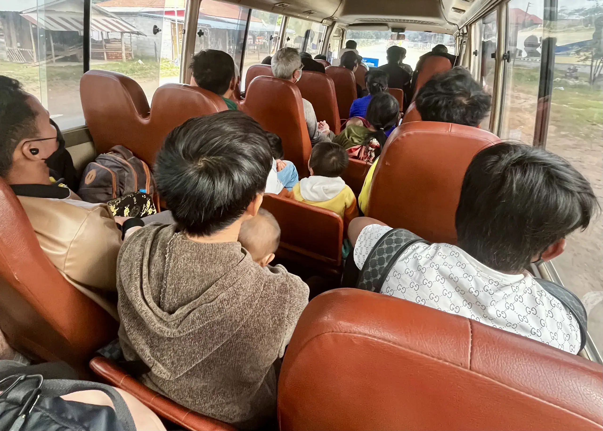 Trekking in Luang Namtha: What to Expect and How to Book 9 A packed public bus going from Huay Xai to Luang Namtha, Laos. The bus has brown leather seats and chairs that fold down into the aisle for extra seats. The people on the bus are sitting very closely together.