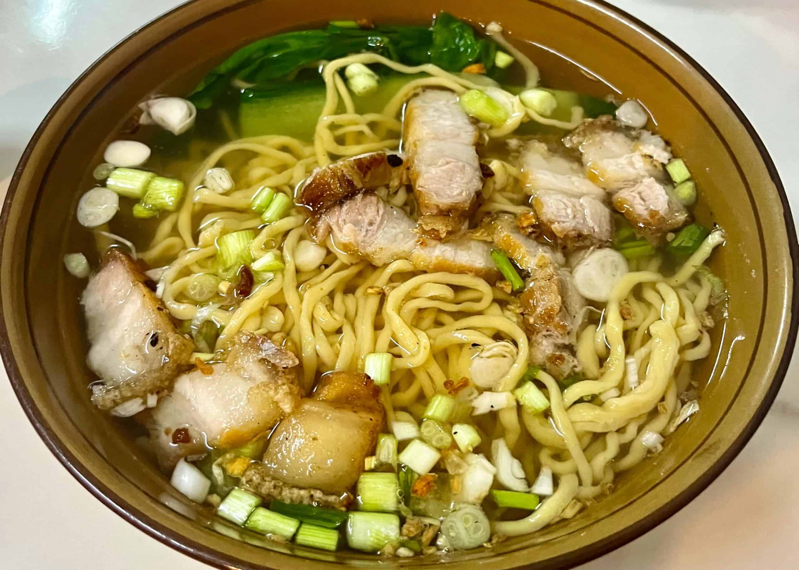 A bowl of yellow noodles with crispy pork and vegetables served in a restaurant in Pakse, Laos.
