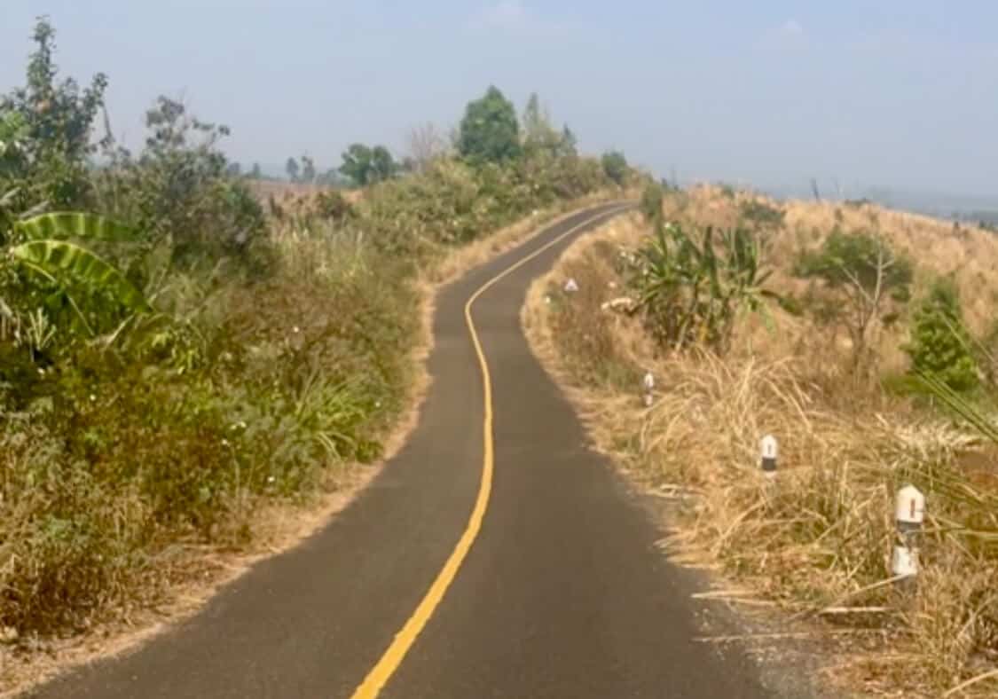 Motorbiking in Laos: Routes, Rentals, Costs & Safety Tips 3 A winding road that disappears over a hill in Laos. The road is marked by a yellow line and there are green bushes around the road