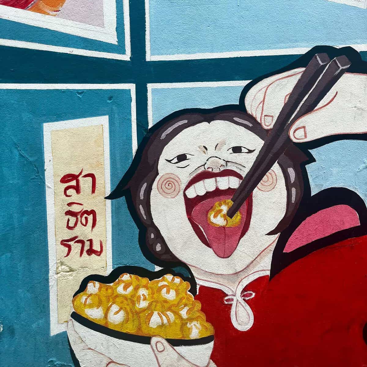 BEST Food in Chinatown Bangkok: What is Actually Worth It 13 Wall art of a person eating a bowl of noodles with chopsticks. Their mouth is open wide.