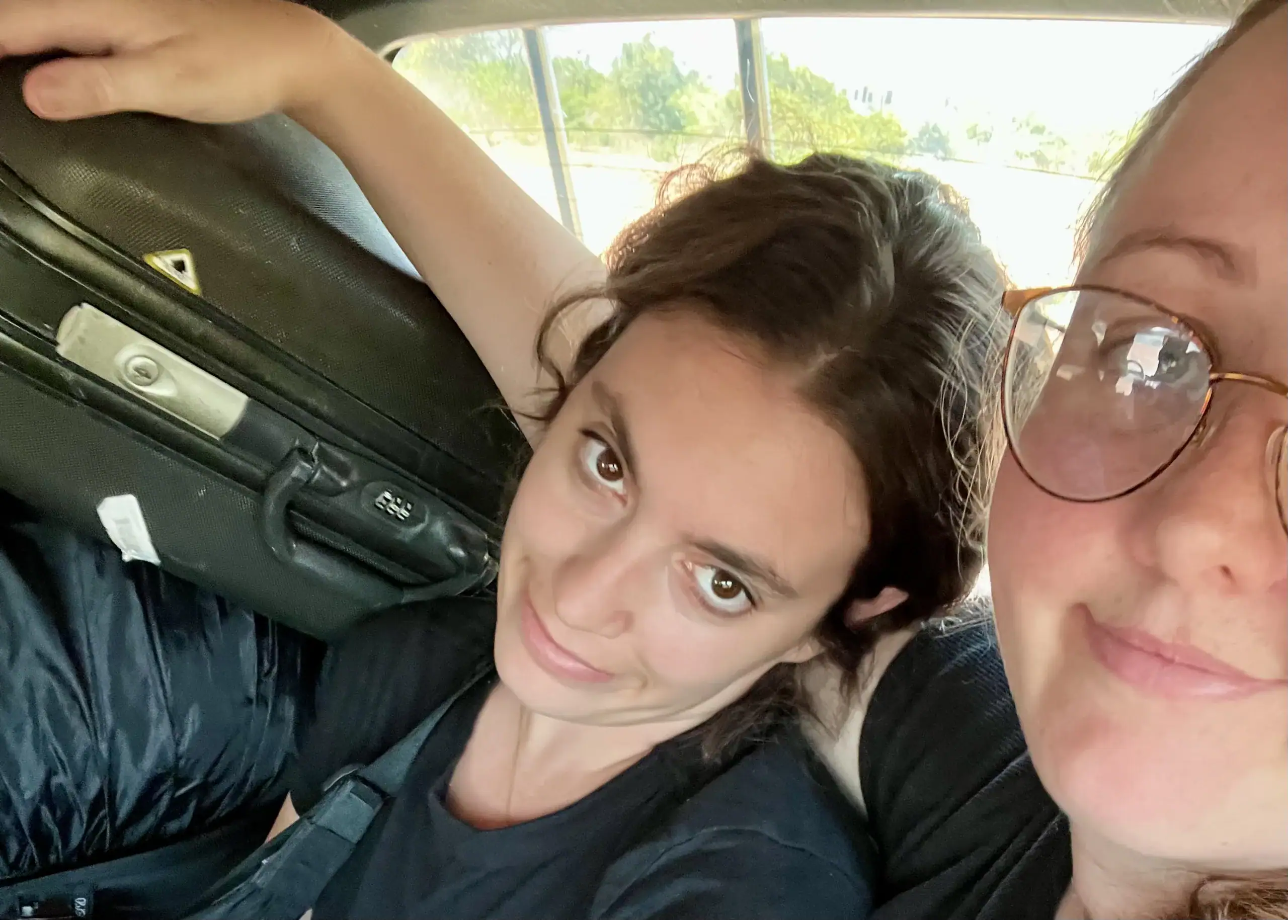 A picture of two girls smiling sarcastically in the back of a minivan in Laos. One girl has her arm around the other as they are surrounded by suitcases