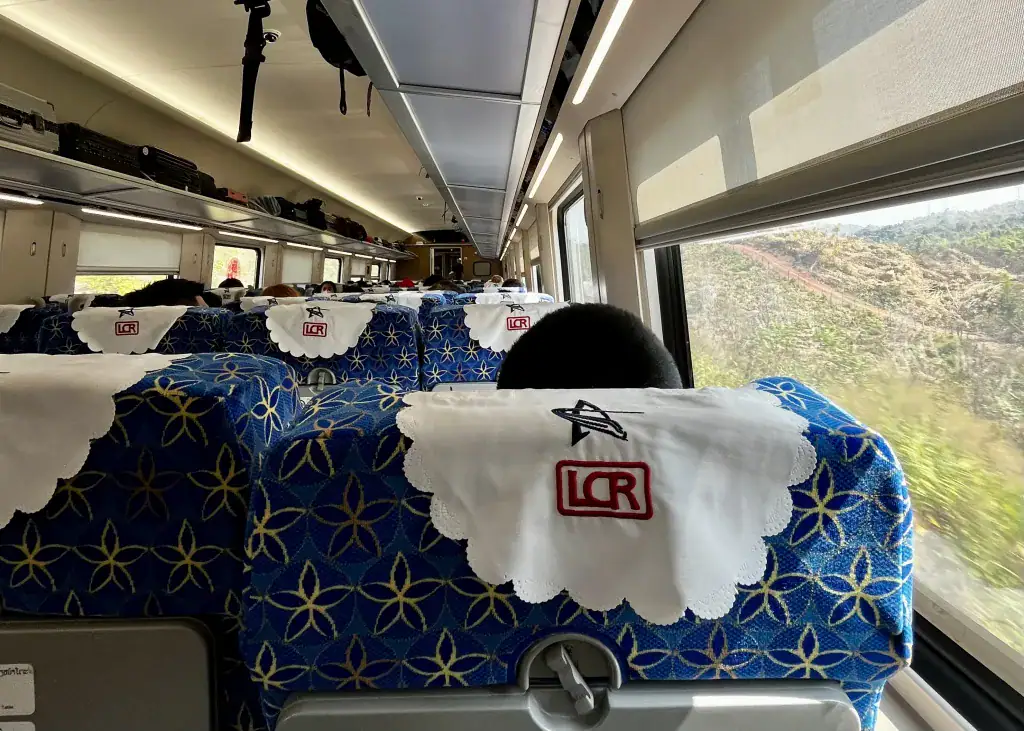 A view from the seat of a train in Laos. The seat is blue with a white cloth over the top stating the train company name "LCR"