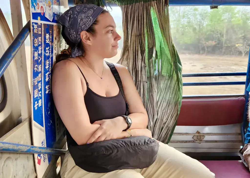 Laos or Vietnam: How to Choose the Best Country for Your Trip 18 A pretty woman wearing a bandana she is glad she added to her Southeast Asia packing list. She is looking out of the songthaew she is travelling on the public transport in Laos. It is a red bench built into the back of a pick up truck