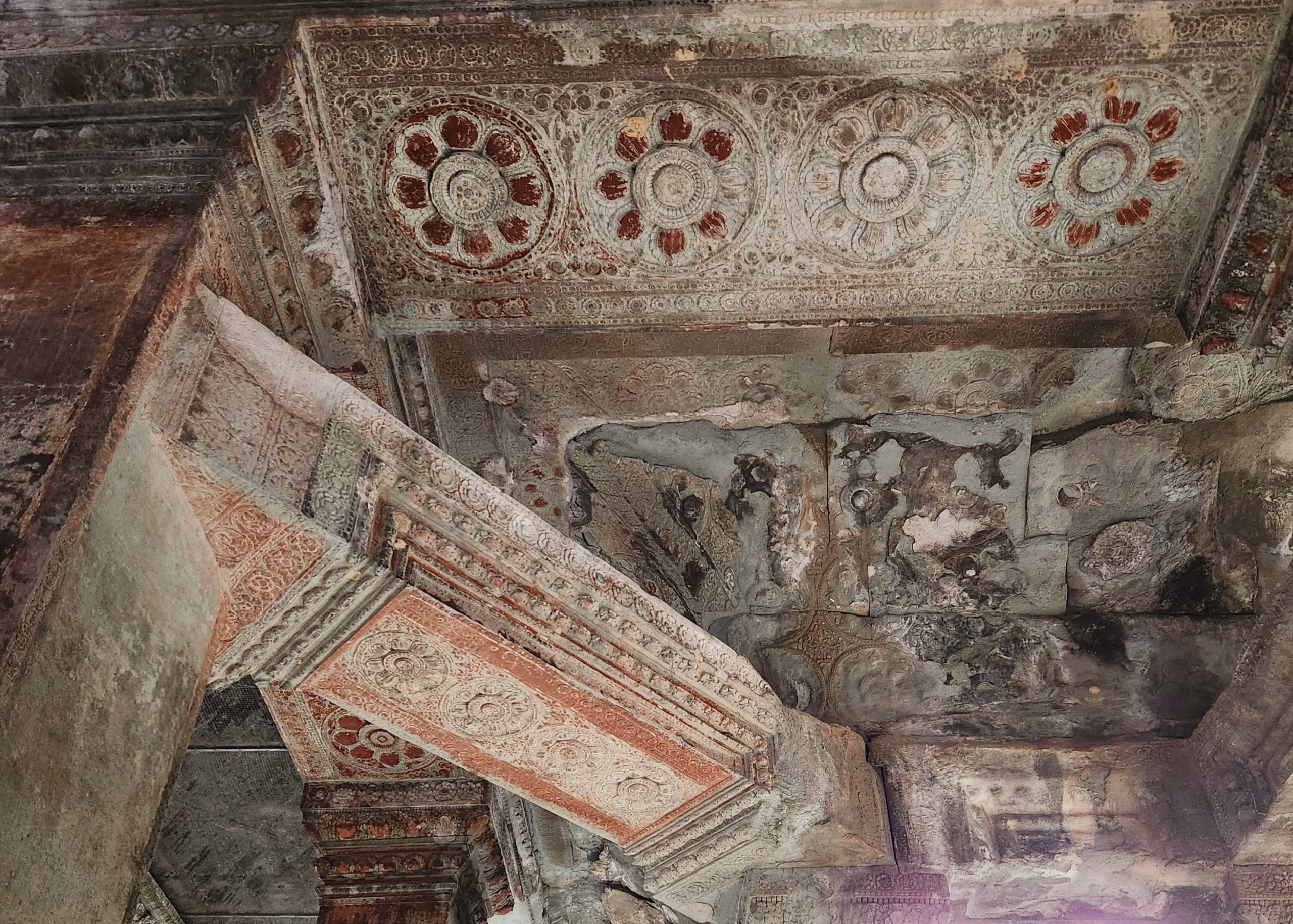 Best Angkor Wat Tour for Sunrise - Our Top Picks 5 A close up of the walls in angkor wat. the stone is painted with patterned red motifs.
