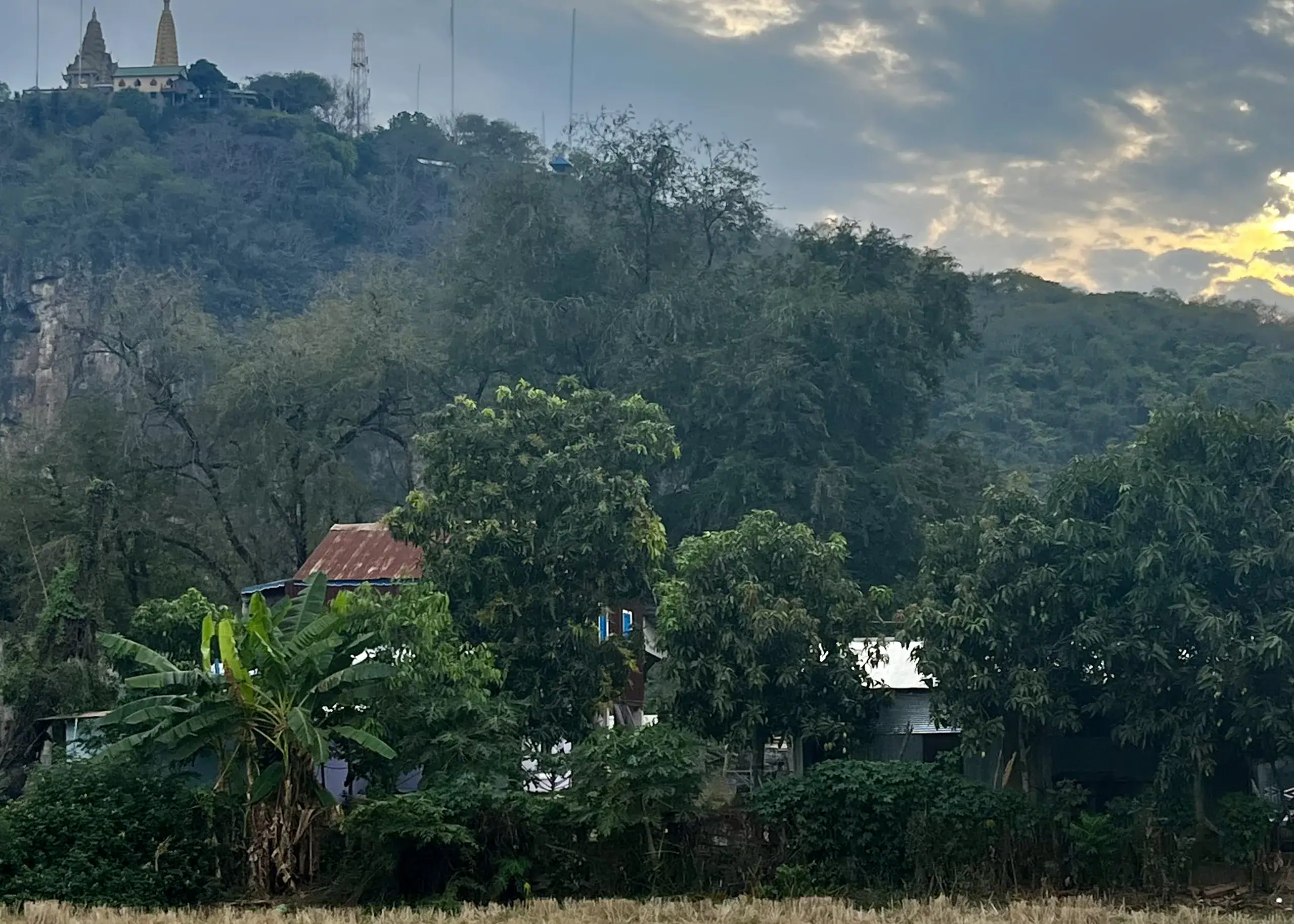 11 Unique Things to Do in Battambang (Even in the Heat!) 3 A view of a temple on a hill. There is a house hidden behind lots of trees and the landscape is very luscious and green at a homestay in Battambang