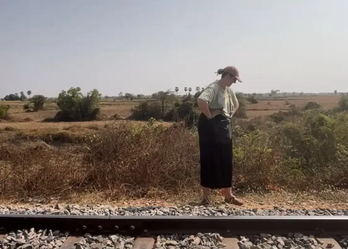 11 Unique Things to Do in Battambang (Even in the Heat!) 1 A woman is stood with her hands on her hips in the Cambodia countryside at the side of a train track.