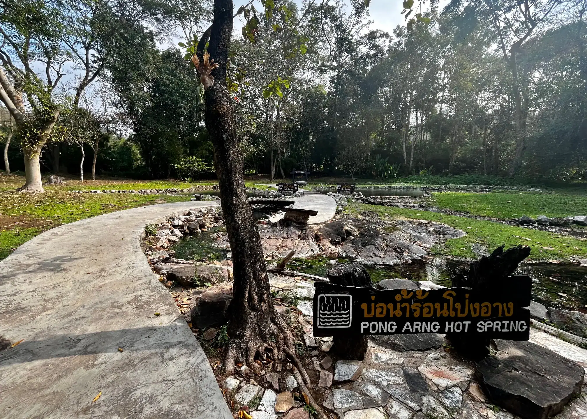 Is Pai Worth Visiting? Where We’d Go Instead 3 A sign says Pong Arng Hot Spring and there is a cement path to the left of the sign leading to the hot springs