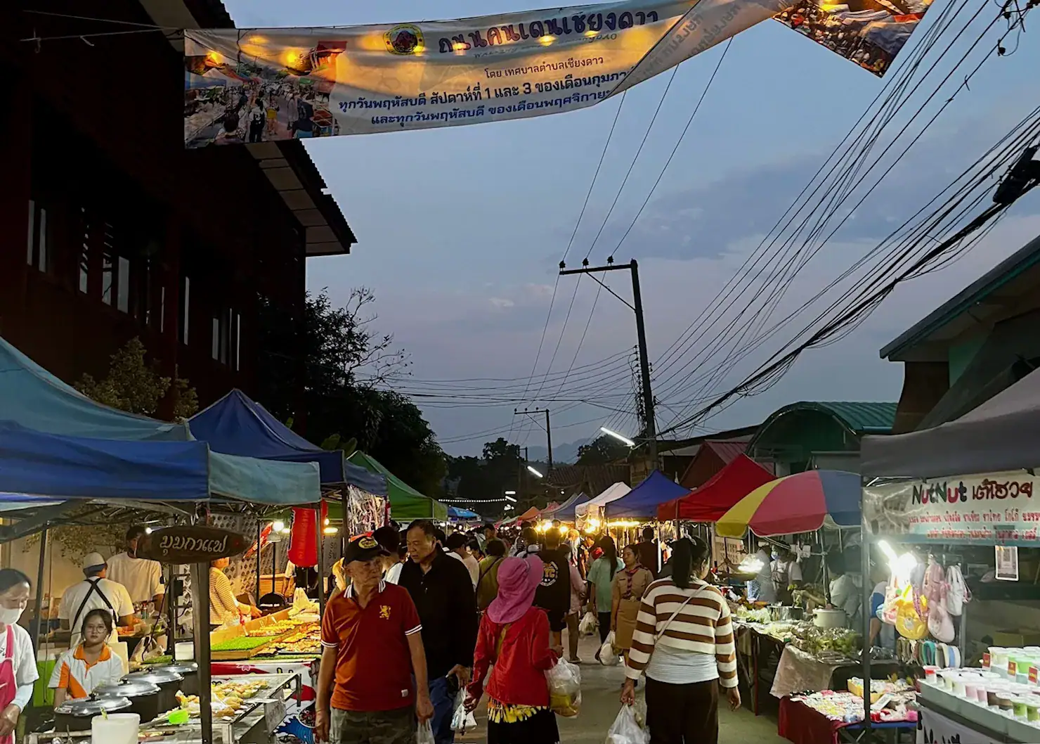 Is Pai Worth Visiting? Where We’d Go Instead 2 A picture of a night market in Chiang Dao. Stalls with colourful umbrellas line the streets. Stalls are selling food, with smoke coming from some stalls. People are walking up and down browsing the stalls