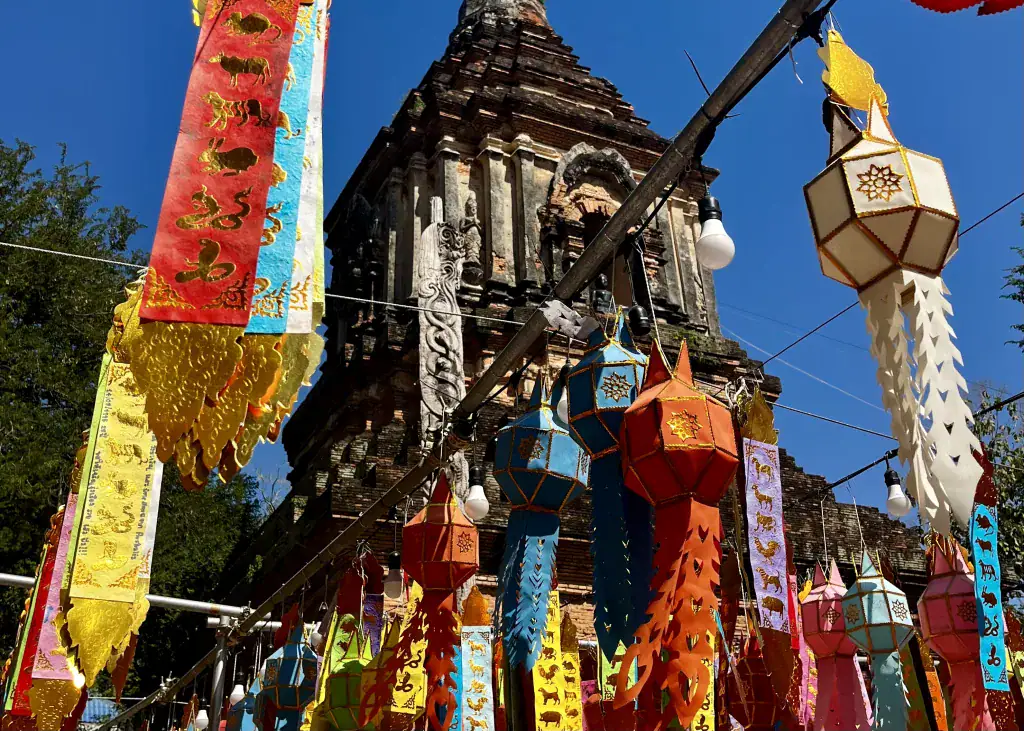 Bangkok to Chiang Mai Travel Guide — How to Get There by Train, Bus & Plane 8 Multi-colored prayer flags are in the foreground, with a dark stone temple in the background in Chiang Mai, add to your itinerary for 10 days in Thailand