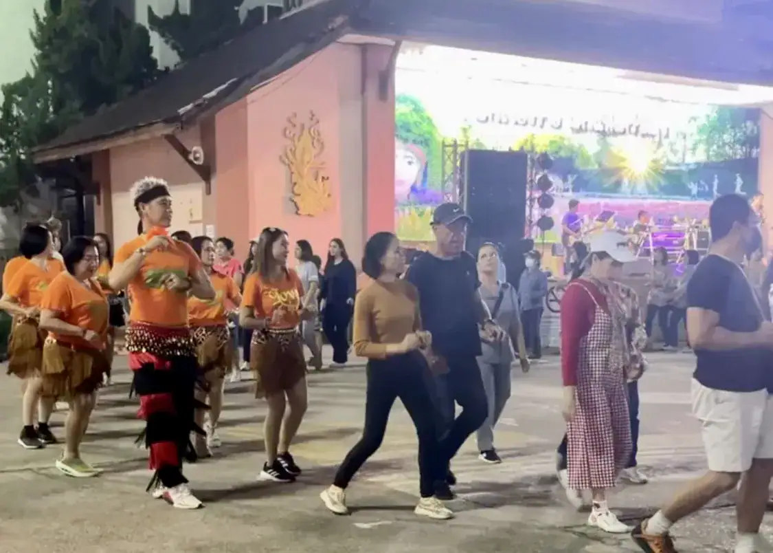 Chiang Mai or Chiang Rai: Which Is Better? 7 People in orange t-shirts are dancing in a circle at a market in CHiang Rai