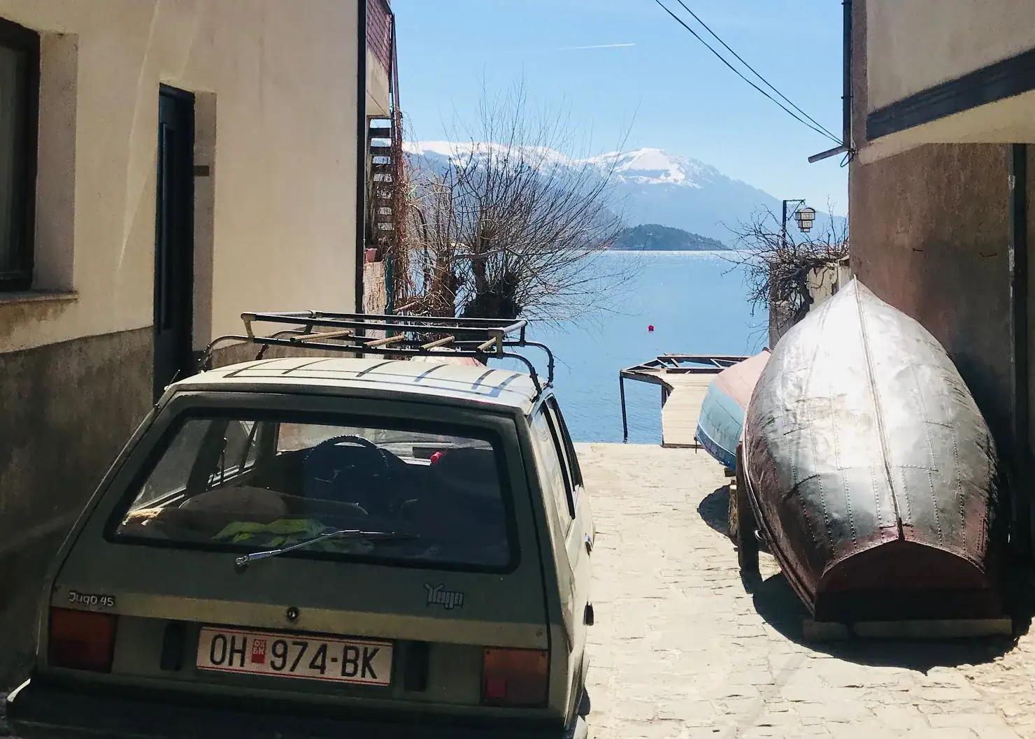 9 Exciting Things To Do in Ohrid, North Macedonia 2 A picture down a side street in Ohrid. THere is a car and a kayak sat down the alley with the lake in the distance