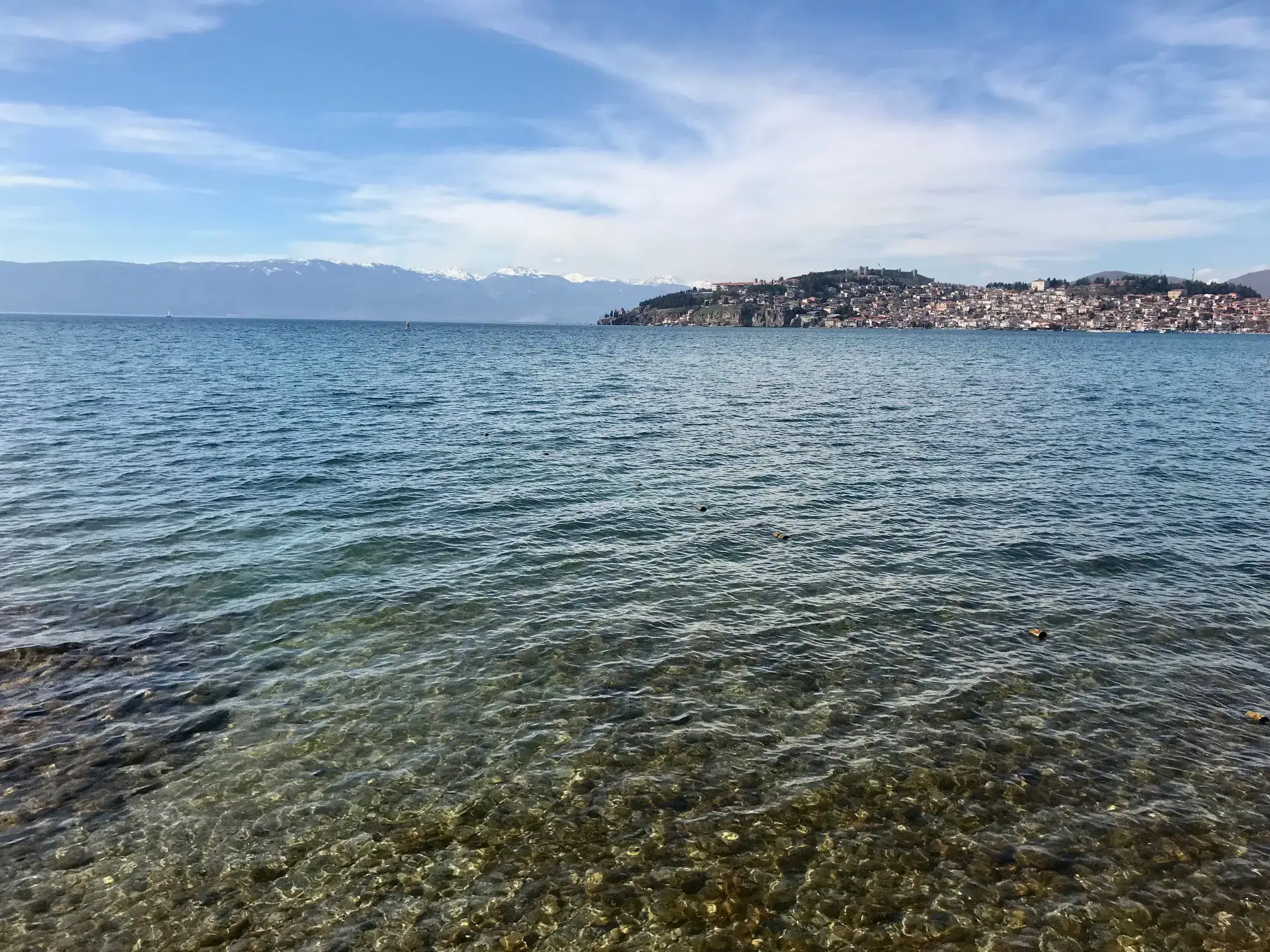 9 Exciting Things To Do in Ohrid, North Macedonia 3 Exploring beaches is on a list of things to do in Ohrid. The lake water is crystal clear with pebbles below. In the background there is a mountain