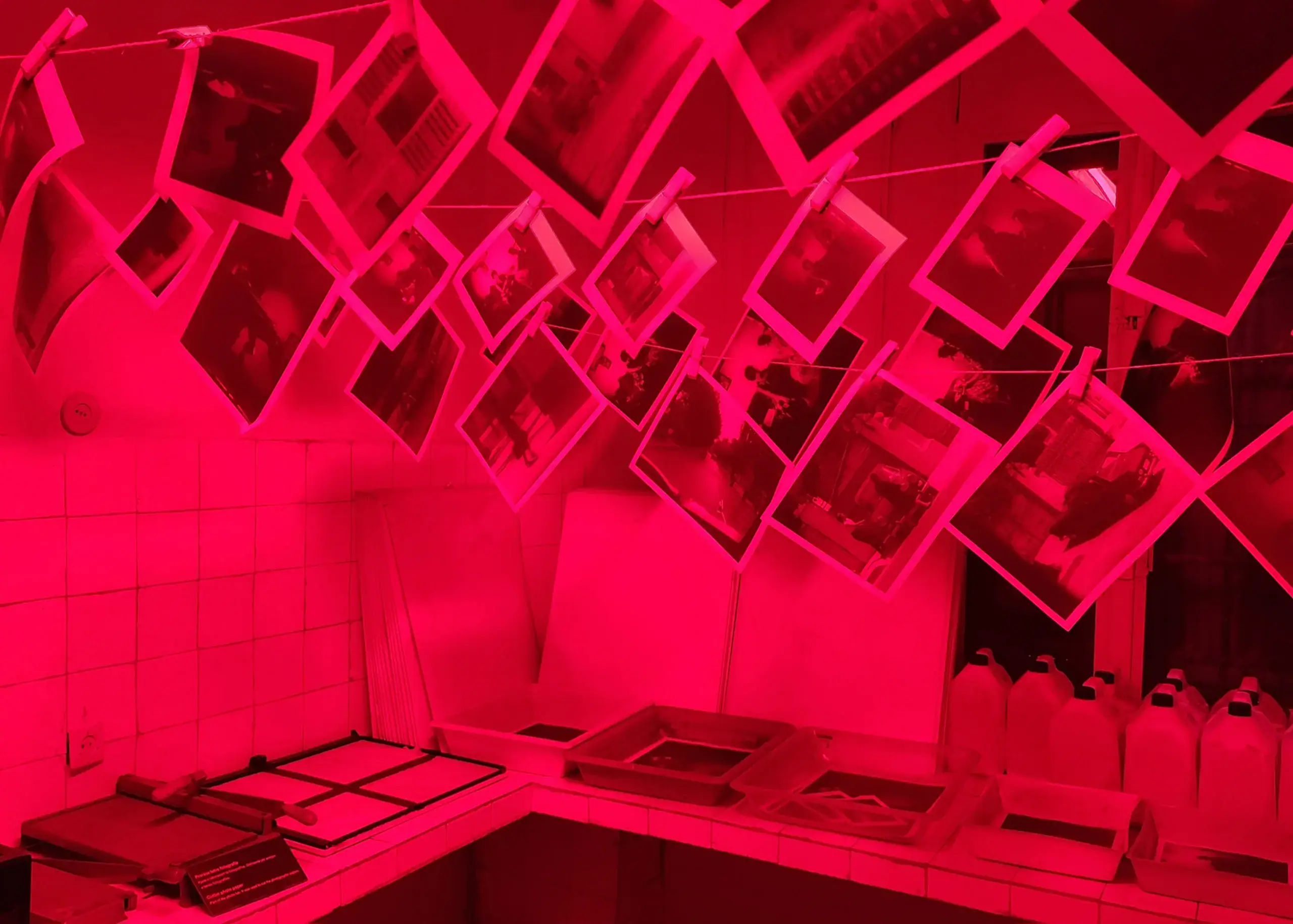 The picture is taken from a red room in House of Leaves Museum, Tirana. There is about twenty photos hanging from pegs at the top of the image