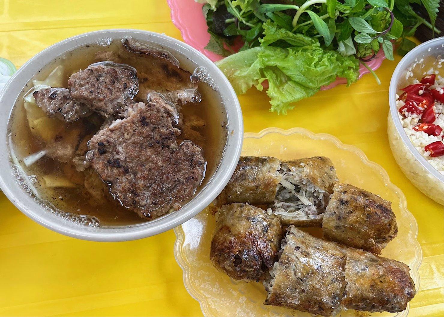 7 Best Places to Go in Vietnam (And What They’re Really Best For) 5 A serving of Bun Cha is sitting on a bright yellow table at a Bun Cha Dac Kim in central Old Quarter Hanoi. There is a bowl of brown broth with sliced beef and noodles, a plate of spring rolls, a plate of herbs, and a bowl of dipping sauce with red peppers in the frame.