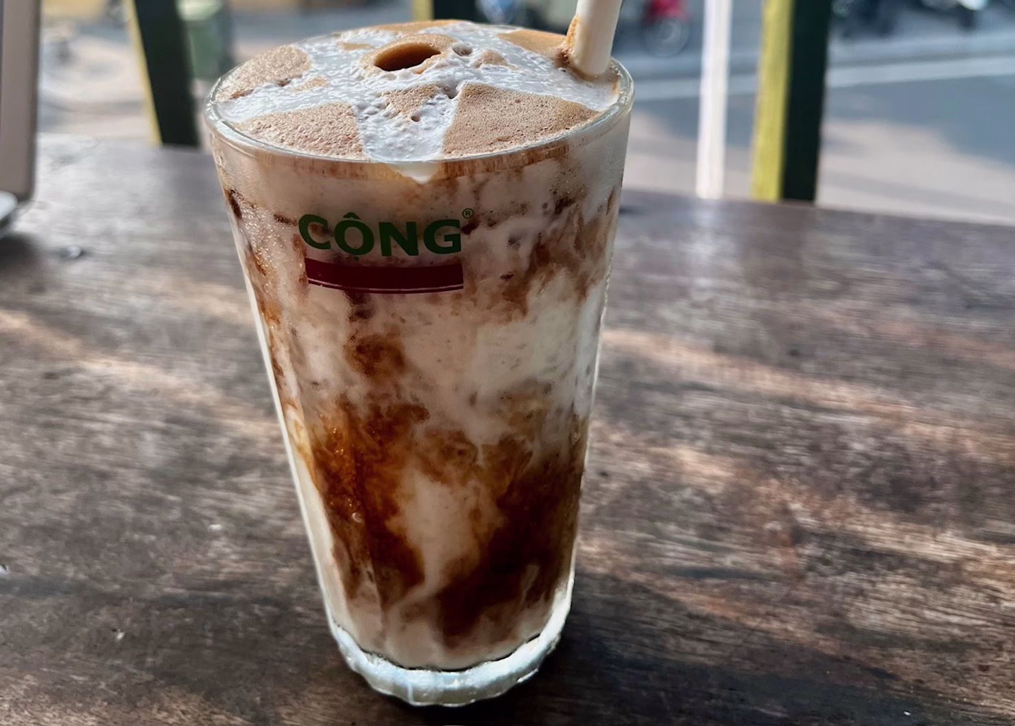 Famous Coffee in Vietnam: A Traveler’s Guide to 8 Must-Try Vietnamese Coffees 2 A coconut coffee is sitting on a wooden bar in a cafe in Hanoi. The coffee shot is mixing with the coconut and there is a paper straw sticking out of the cup. This is a type of famous coffee in Vietnam.