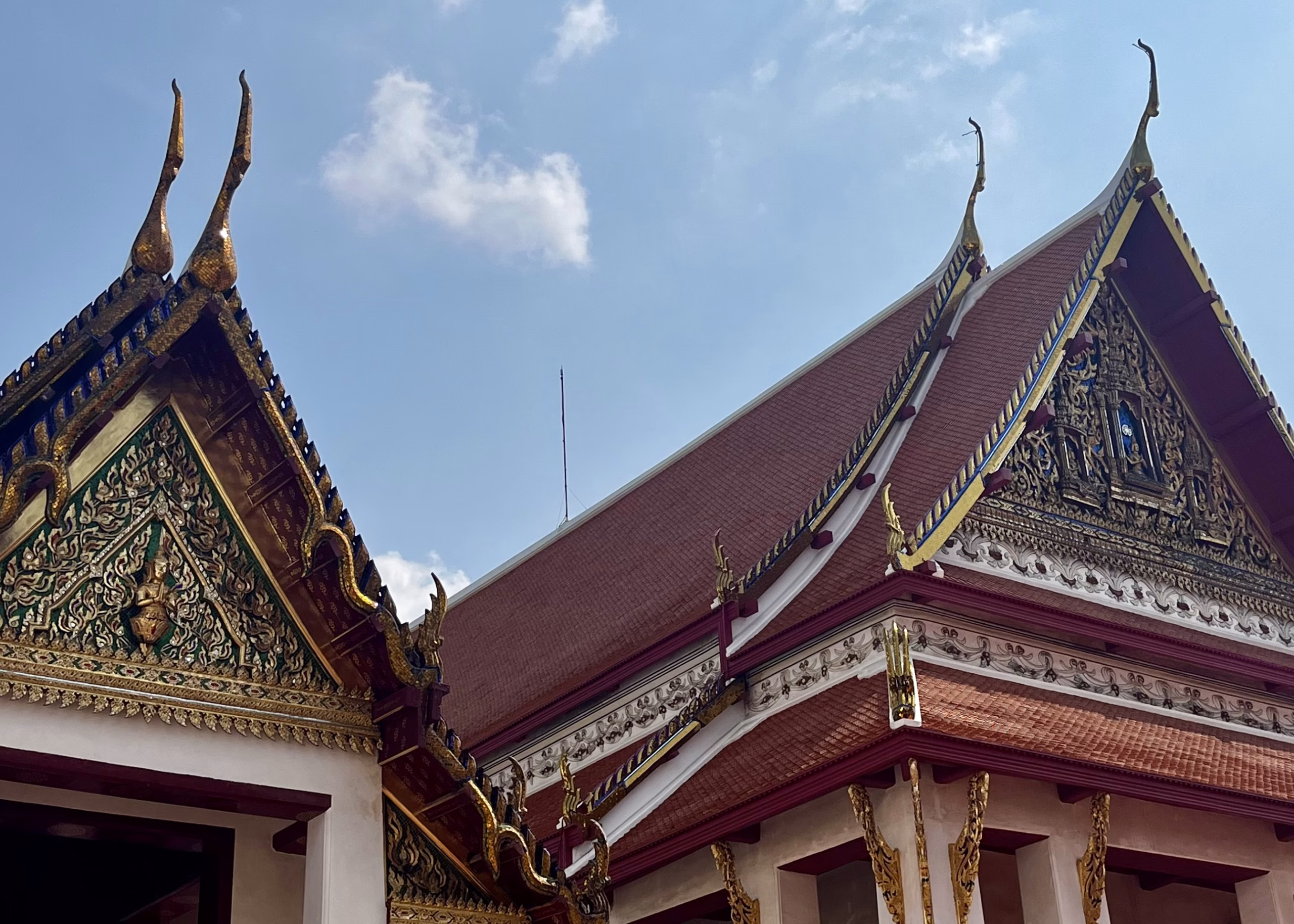 24 Hours in Bangkok: Epic Wats, Local Markets & Street Food 5 An ornate building in classic Thai style is set in front of a clear blue sky. The building has gold gilded paintings on the top and gold points on the roof.