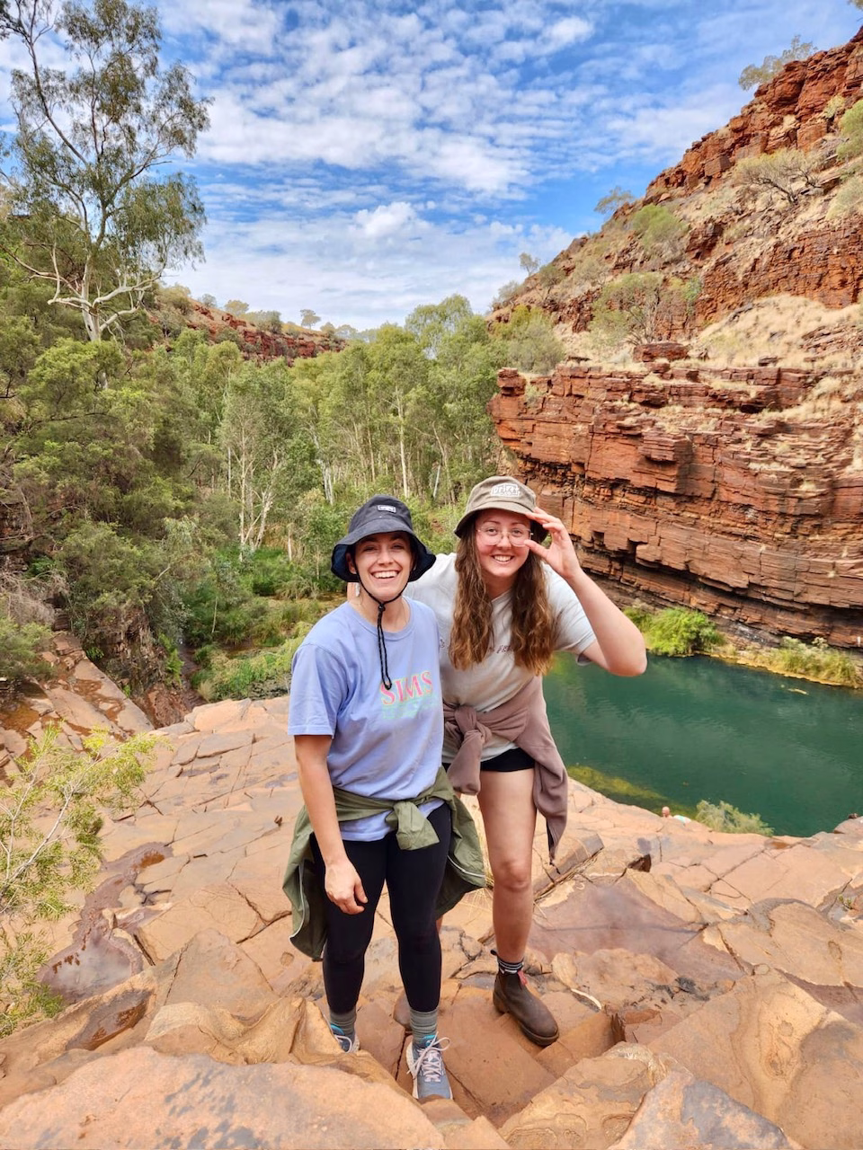 About The Lavender Travelers 7 Two women posing in front of a water hole in Karijini National Park in Australia.