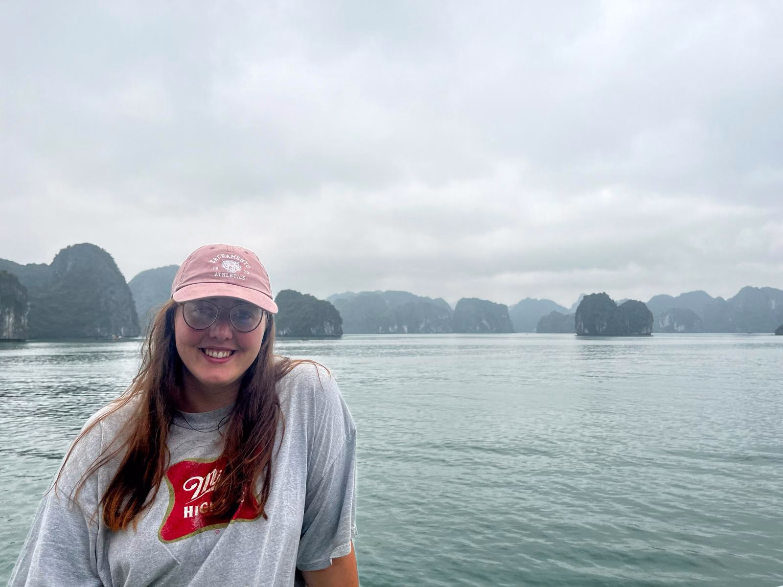 4 Week Vietnam Itinerary: Laid-Back Adventures on a Budget 4 A girl in a red cap is posing from a boat with a view of Ha Long Bay in the background. There are mountains in the background with a misty sky