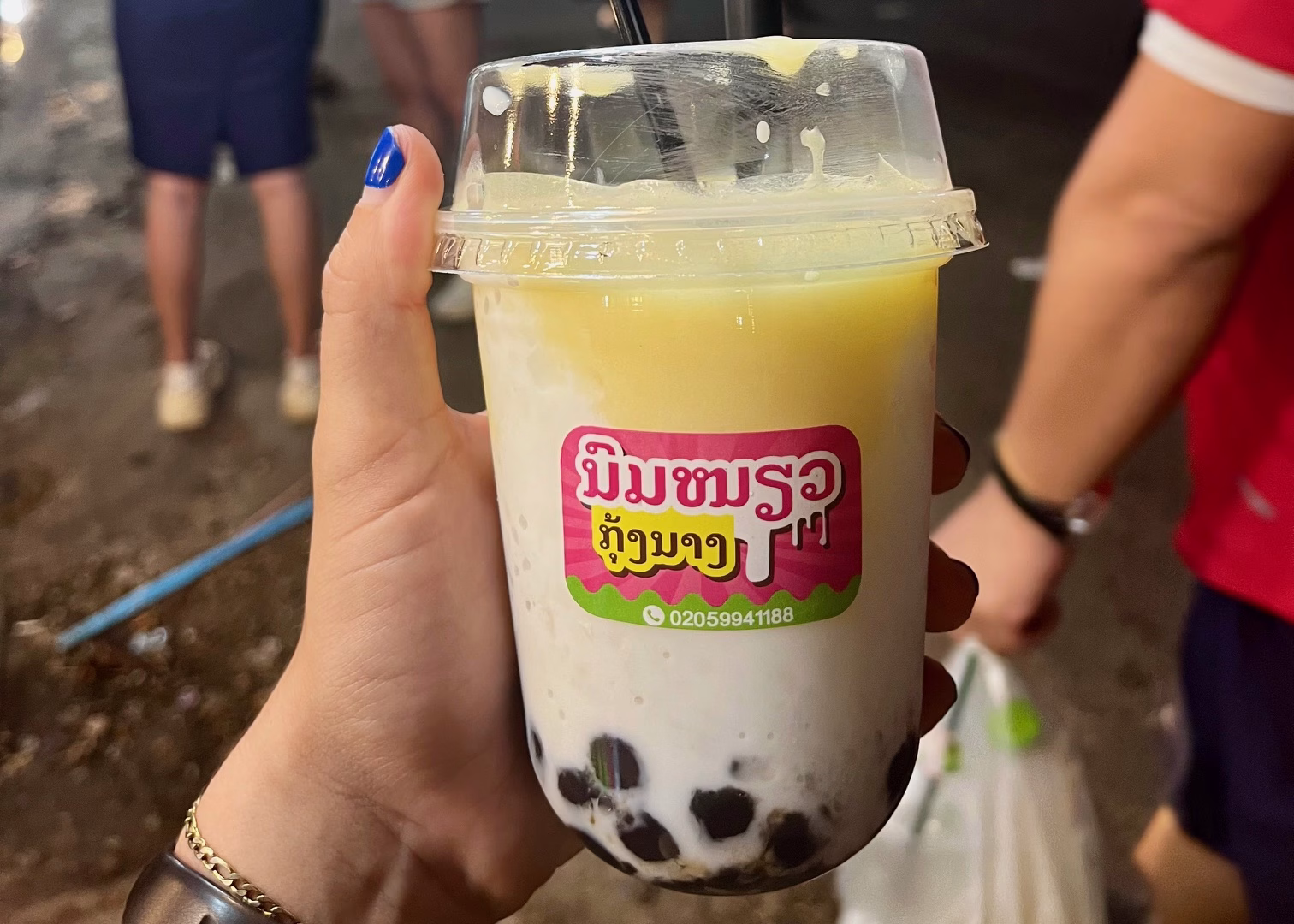 A coconut vanilla pudding drink from the Vientiane night market is held by a woman's hand.