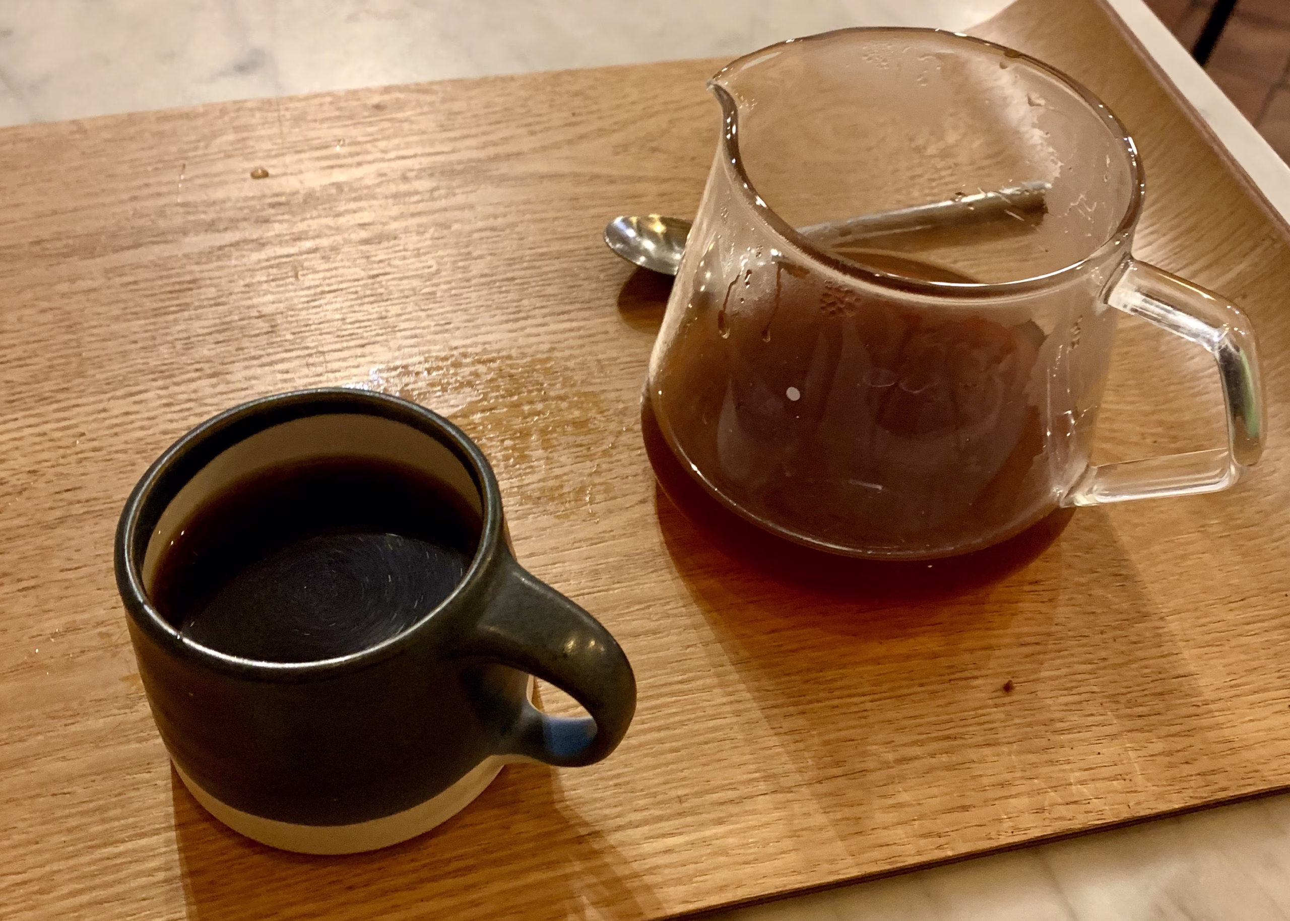Famous Coffee in Vietnam: A Traveler’s Guide to 8 Must-Try Vietnamese Coffees 8 A fancy looking cup of coffee in a black mug is sitting on a wooden board. There is a glass decanter that the coffee was brewed into sitting next to the mug.