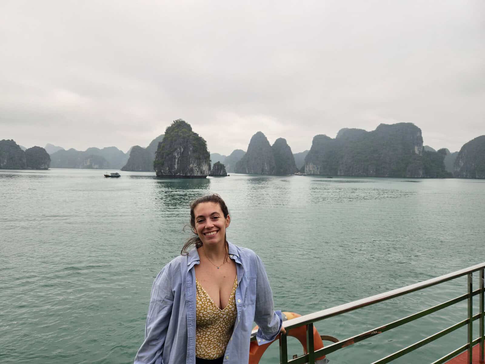 Halong Bay Budget Cruise Guide: Top Picks + How to Save Big 10 A woman in a swimsuit and button up shirt is smiling in front of the scenery on Halong Bay.