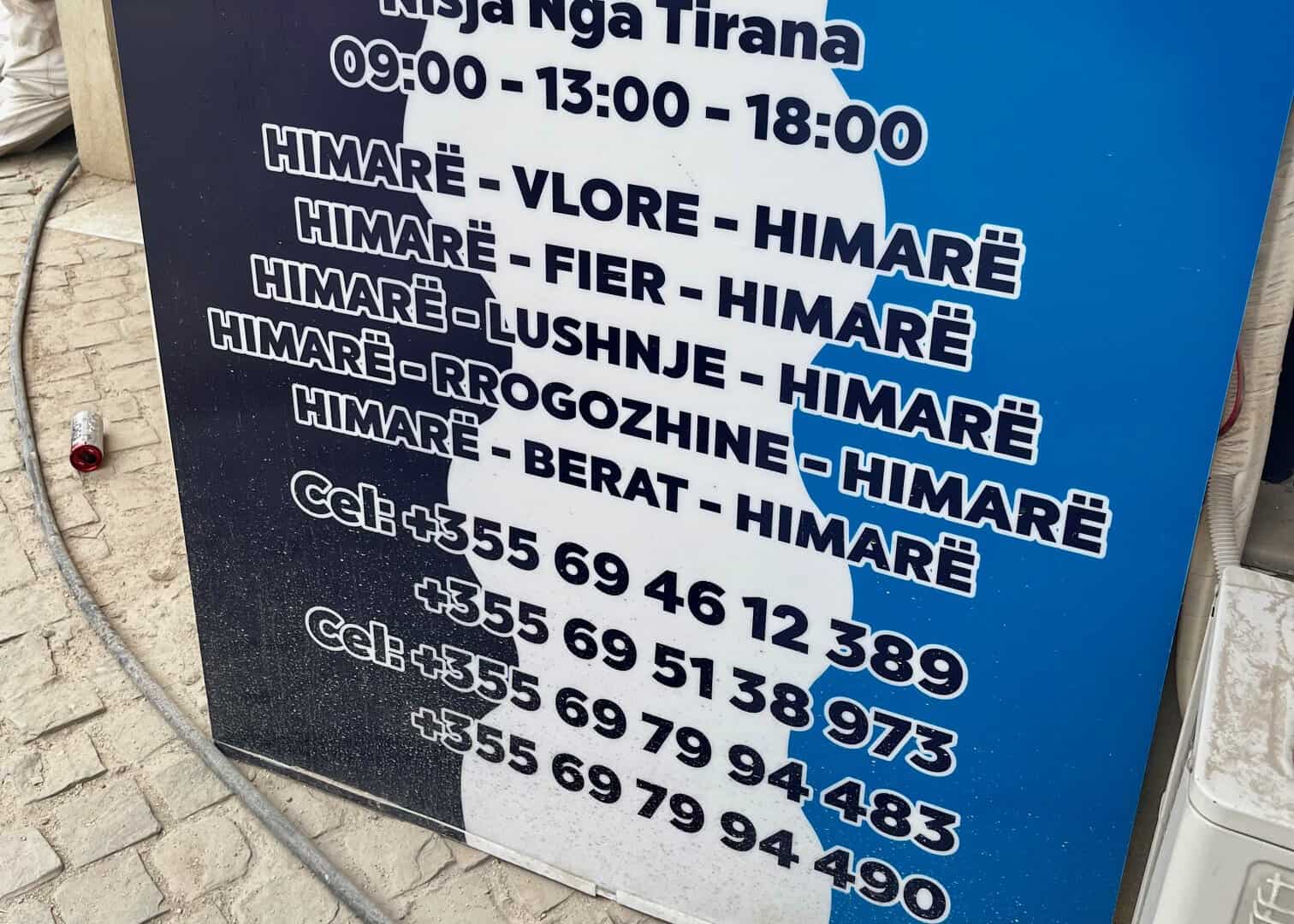 10 Best Himarë Beaches: Local Tips & Hidden Gems 10 A photo of a sign in Himarë showing the local bus routes and times with Whatsapp numbers to contact the bus agency.