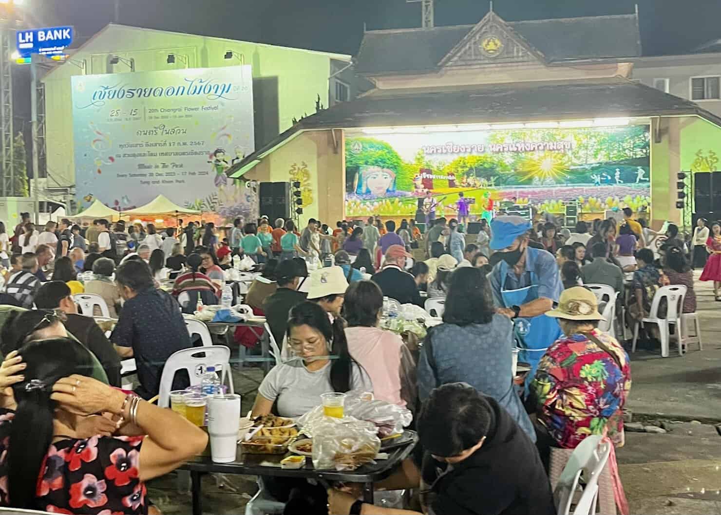 A crowd at the Chiang Rai night market sitting at plastic tables across from the stage.