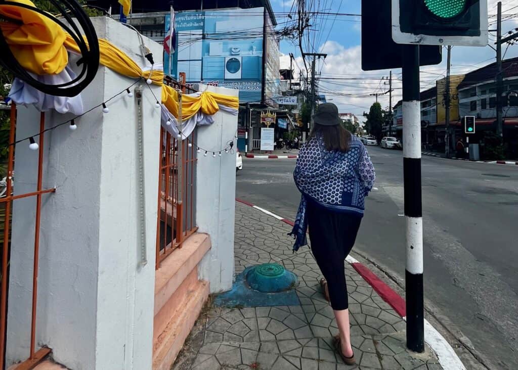 A woman with a blue scarf around her shoulders is walking down the sidewalk in Chiang Rai.