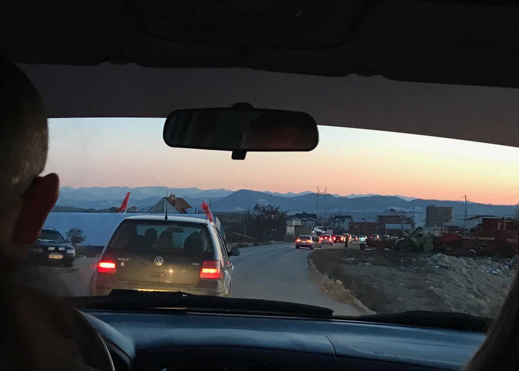 A close up of the sunset in a taxi in Albania through the front windscreen. There are many cars on the road in front and the drivers head is to the left side in the photo.