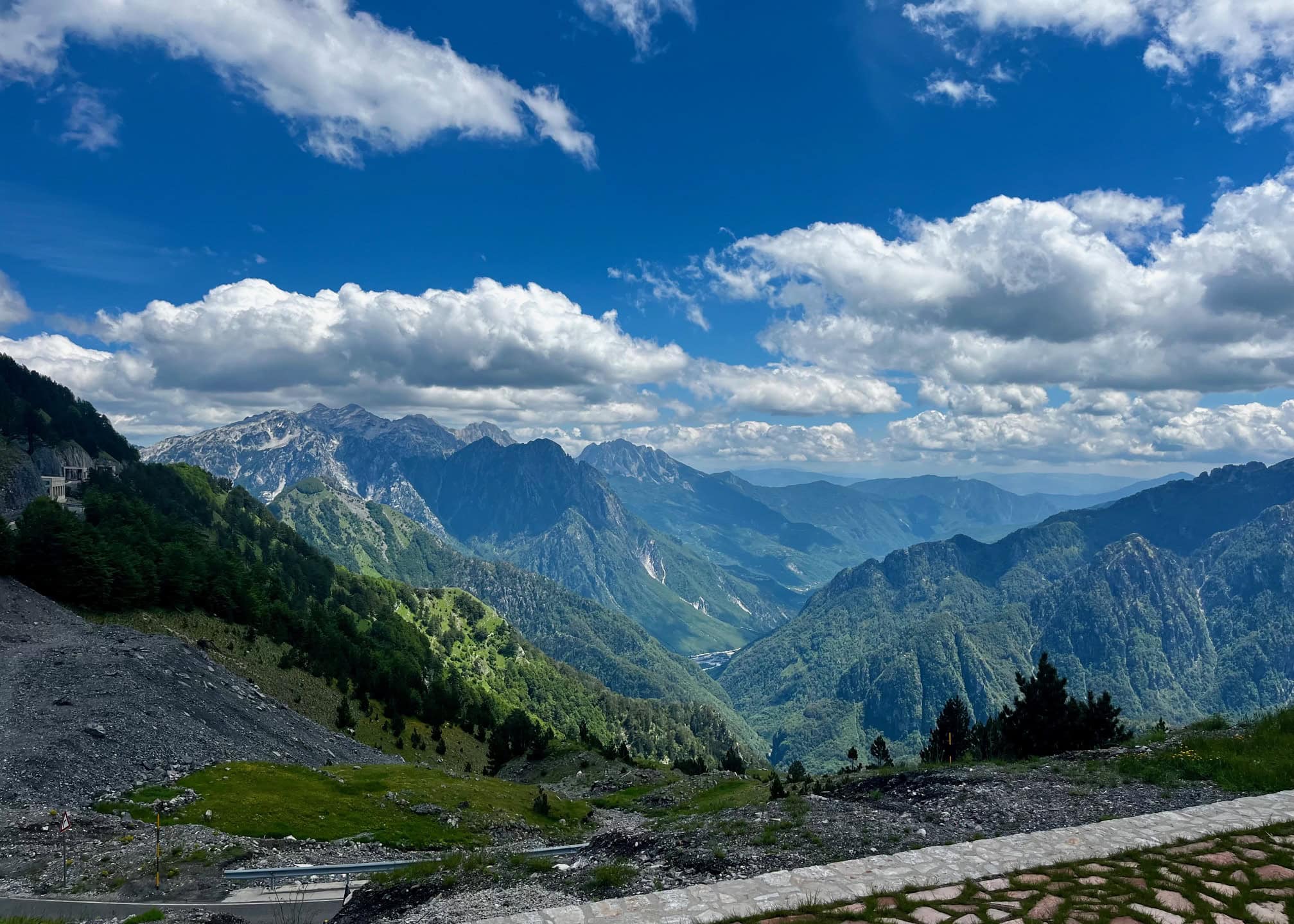A view of green and blue layered mountains is in the distance at a viewpoint on the drive from Shkoder to Theth.