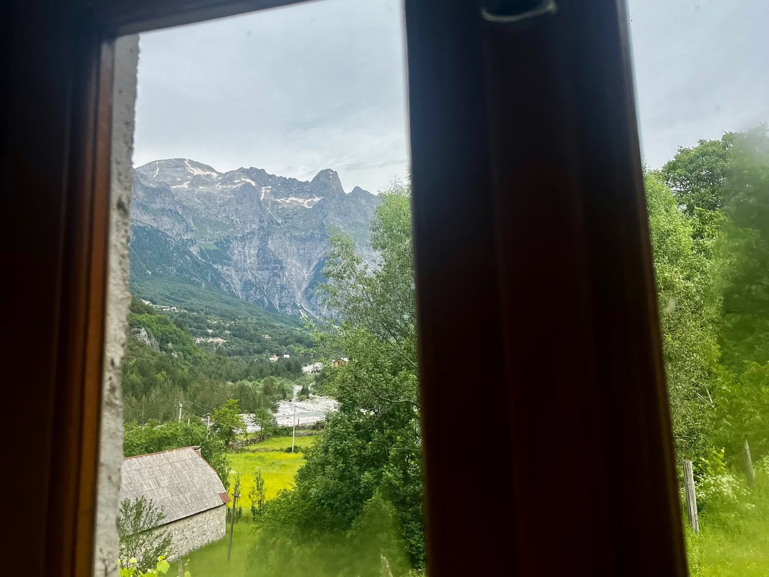 Where to Stay in Theth: Best Value Guesthouses 7 The view out the window from a guesthouse in Theth framed by a brown window frame.