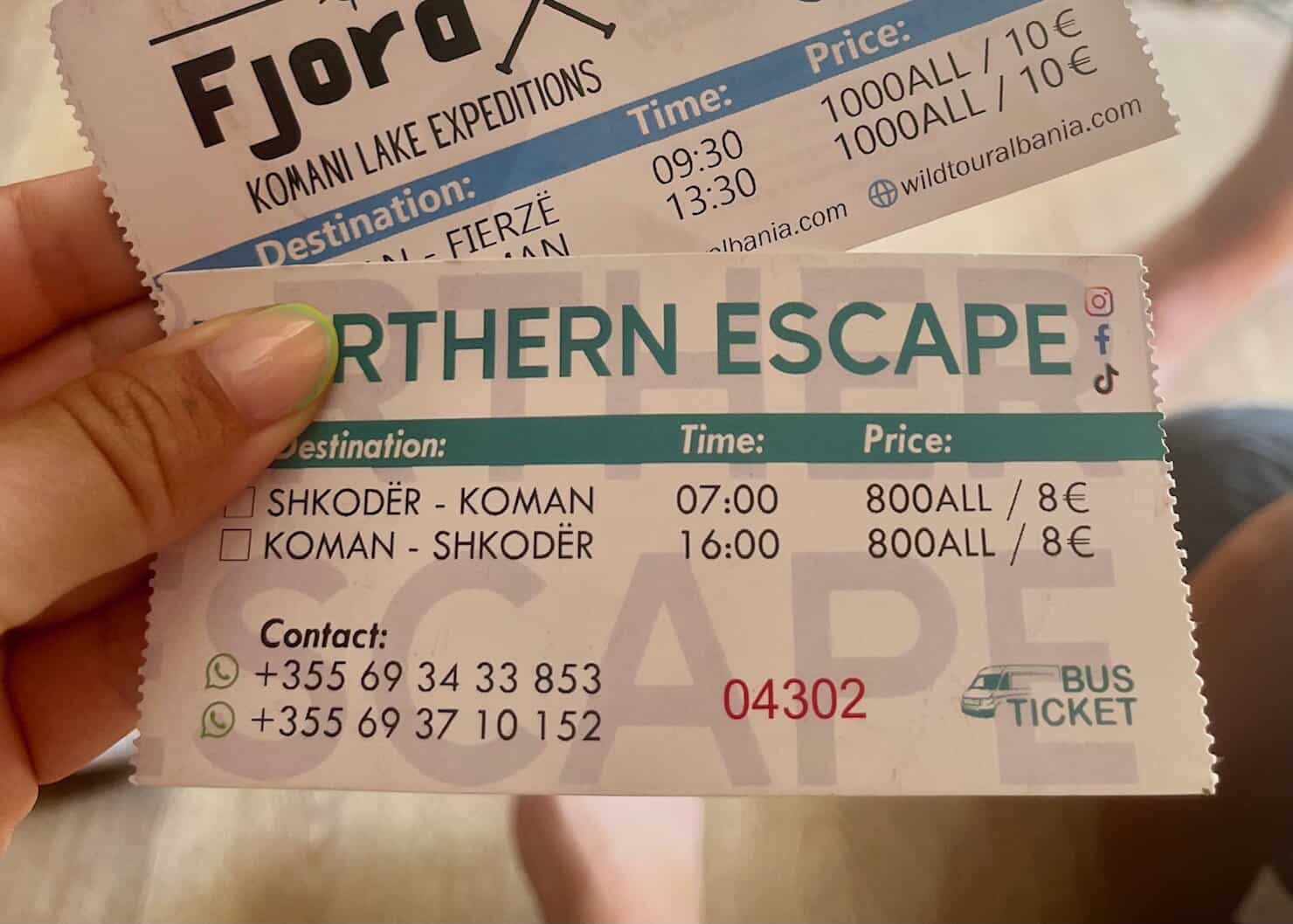 A white and green bus ticket with the heading Northern Escape is held by a women with pink painted nails. The ticket is for Komani to Shkoder which is one of the bumpier Albanian buses to ride.