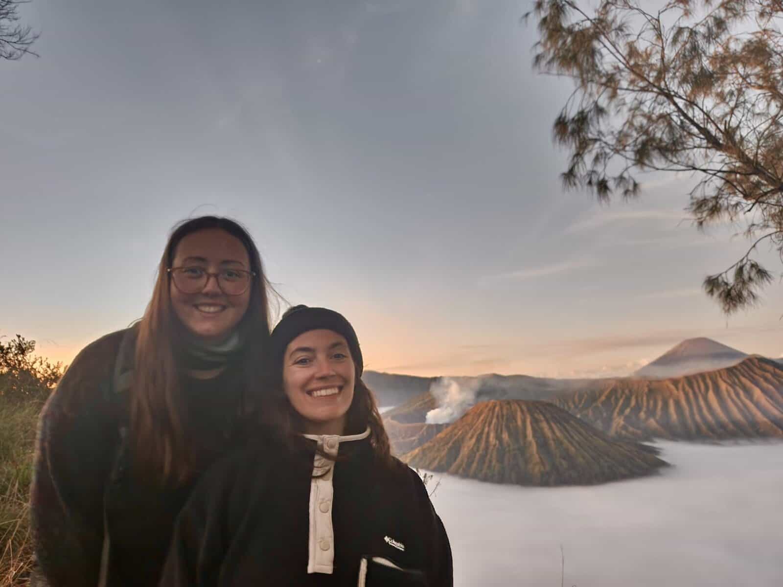 Destinations 1 Two women are smiling standing at a viewpoint above Mt Bromo while watching the sunrise.