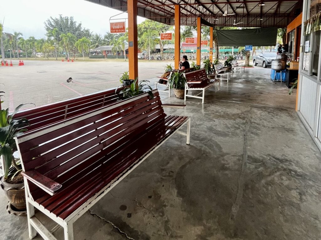 Where to Stay in Chiang Dao: 3 Best Areas & Top Picks 10 The bus station in Chiang Dao. The station is concrete, with red benches and orange beams supporting the roof. There are a few people waiting on the benches, but it is empty otherwise