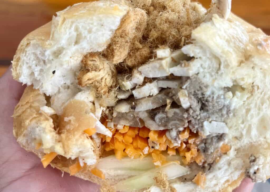 A close up of a Laos sandwich in Vang Vieng, Laos. The sandwich has French bread, carrot, cucumber, pork pate, chicken, and pork floss.