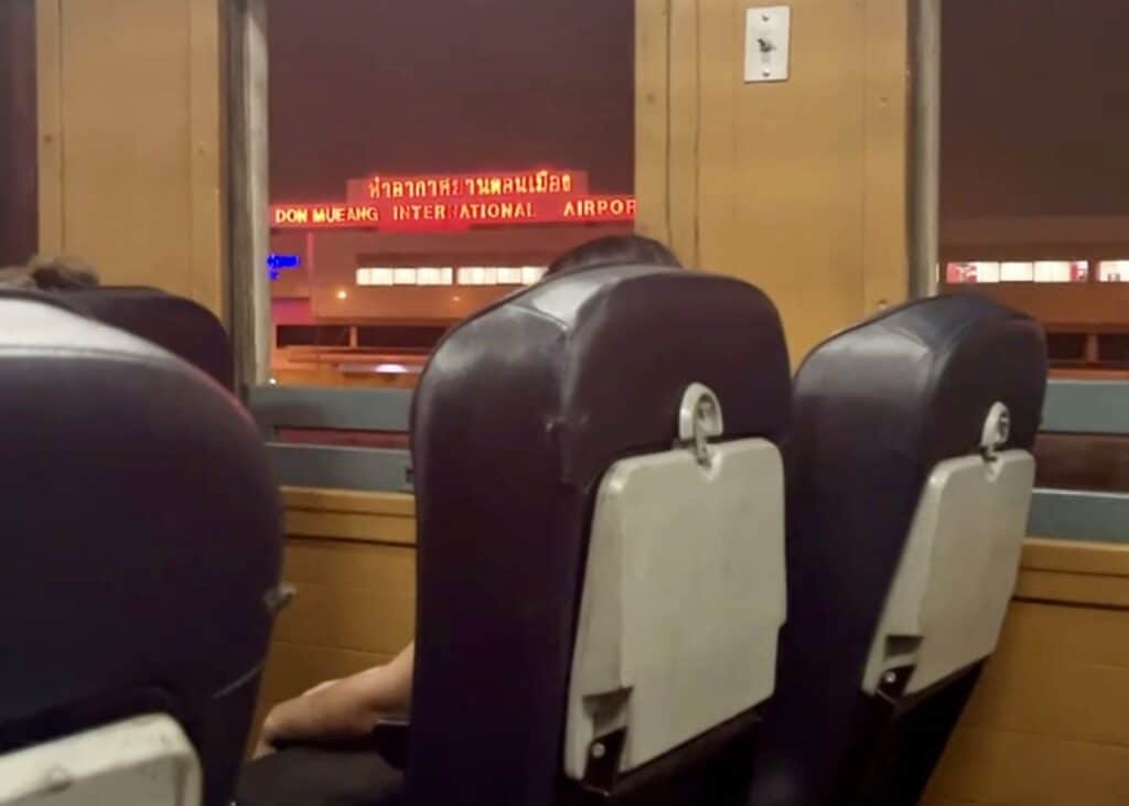 Bangkok to Chiang Mai Travel Guide — How to Get There by Train, Bus & Plane 13 Seats on a train going from Bangkok to Chiang Mai as it goes past Don Meueng Airport outside of the city. The name of the airport is lit up in red neon lights outside the train window.