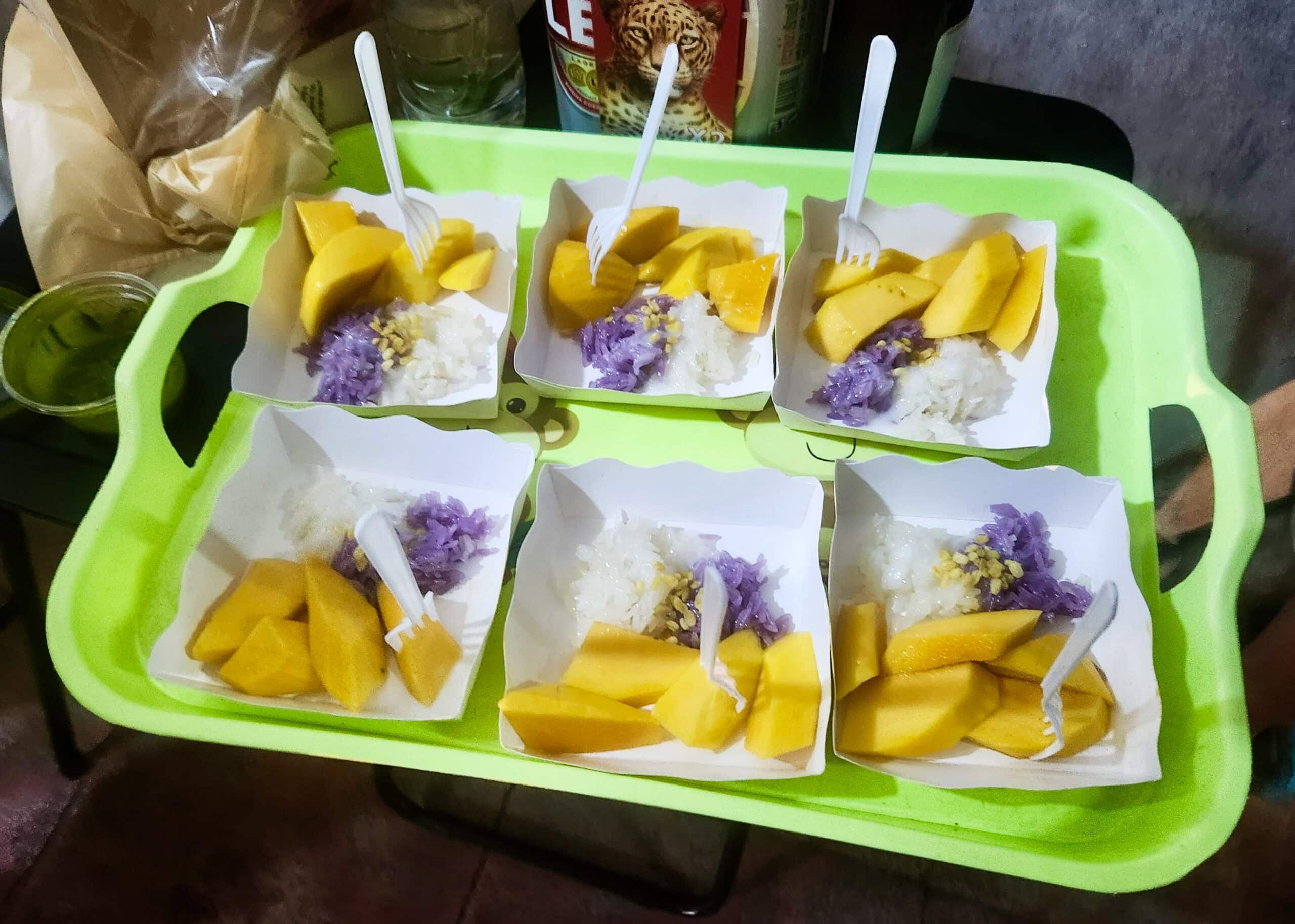 Bangkok Food Tour: Our Honest Review of Chinatown’s Best Street Eats 1 A lime green tray holds 6 mini mango sticky rice servings with small plastic forks stuck in the mango.