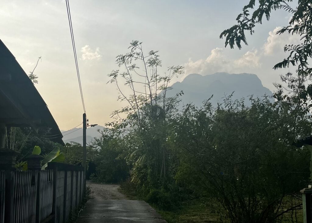 Where to Stay in Chiang Dao: 3 Best Areas & Top Picks 6 A mountain in the distance at dusk sits behind large green bushes along a small road in Chiang Dao.