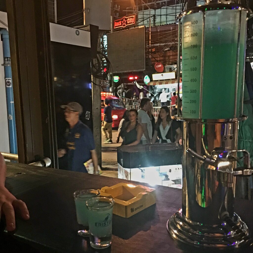 Where to Go in Thailand for the First Time: A Budget Traveler’s Guide 11 The picture shows a container of bright blue alcohol with a leaver to pour the alcohol into the two shot glasses sat next to it