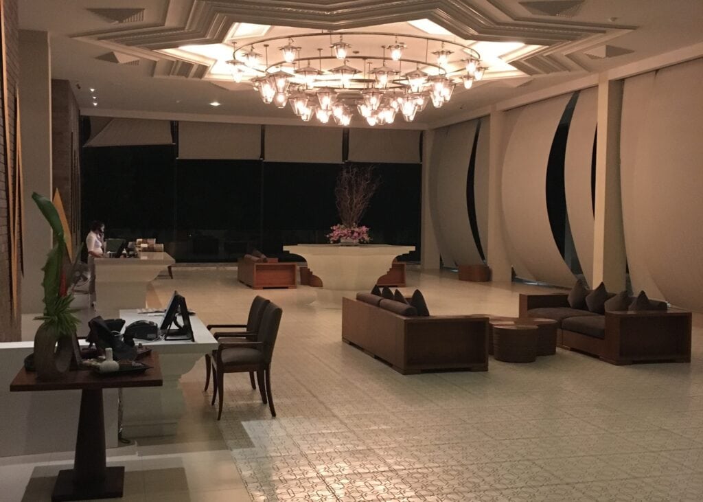 Phuket vs Krabi: Our 20s Party Trip vs 30s Chill Trip 3 The reception/lobby of Avista Hideaway Resort in Phuket. There's a huge lotus flower shaped light fixture, white walls and floors, with brown couches for guests to sit at
