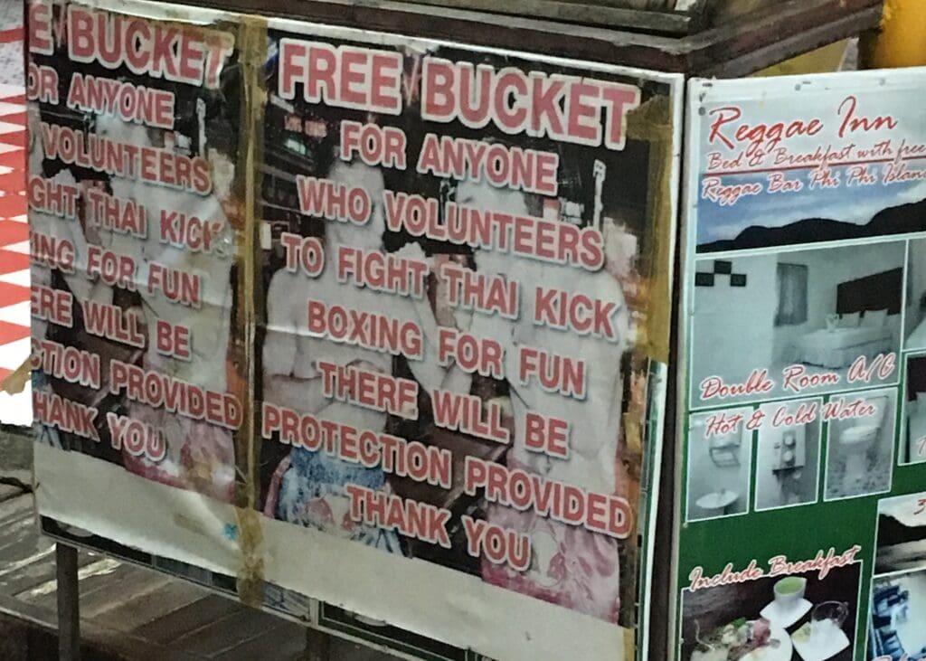 Phuket vs Krabi: Our 20s Party Trip vs 30s Chill Trip 7 A sign on the street in Phuket that highlights it's drinking culture. It says "free bucket for anyone who volunteers to fight thai kickboxing for fun. There will be protection provided thank you."