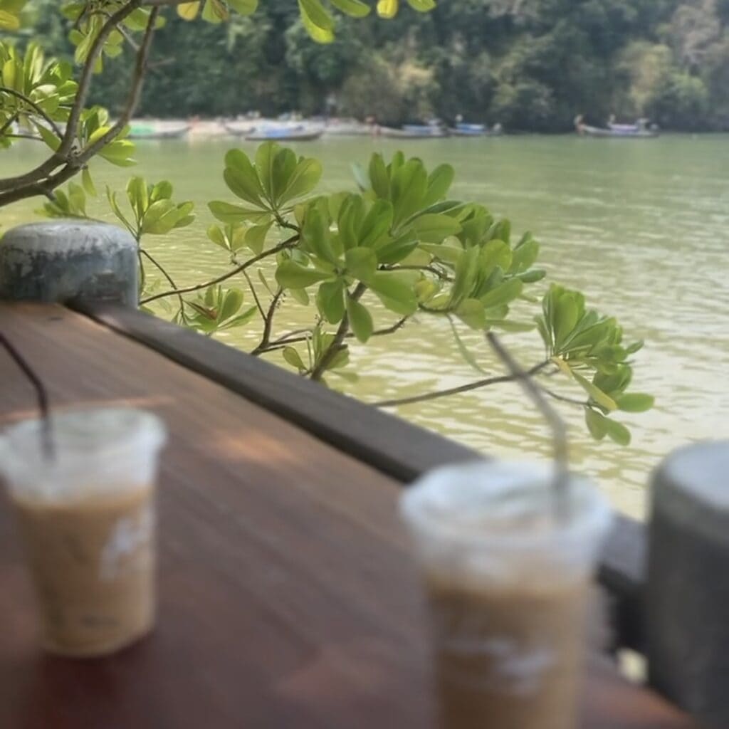 Phuket vs Krabi: Our 20s Party Trip vs 30s Chill Trip 10 Taken from a coffee shop in Ao Nang, two plasctic iced coffee cups sit on the bench with a view of the water and mountains in the background
